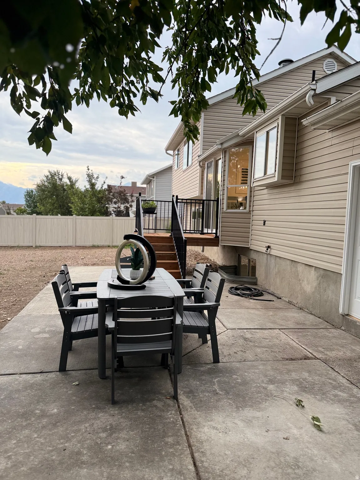 Expansive concrete patio with direct access to a multi-level wooden deck featuring black metal railings