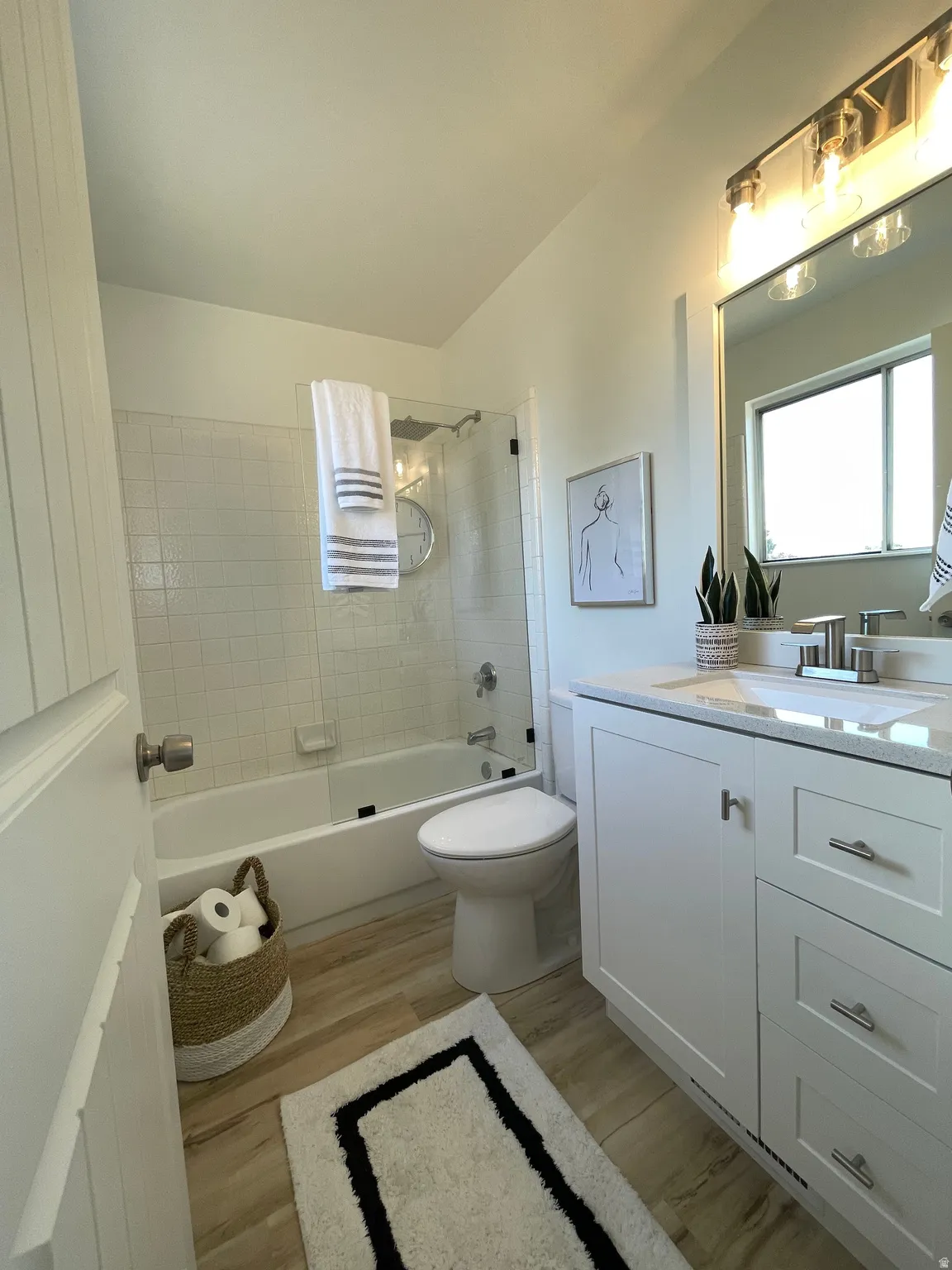 Primary bathroom featuring a tub/shower combination with subway tile surround, white vanity with integrated sink and chrome fixtures, wood-finish flooring.