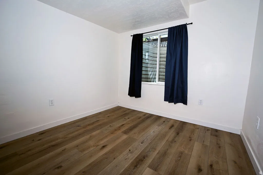 Wood-finish flooring with white baseboards, bright white walls, and a window with dark drapery