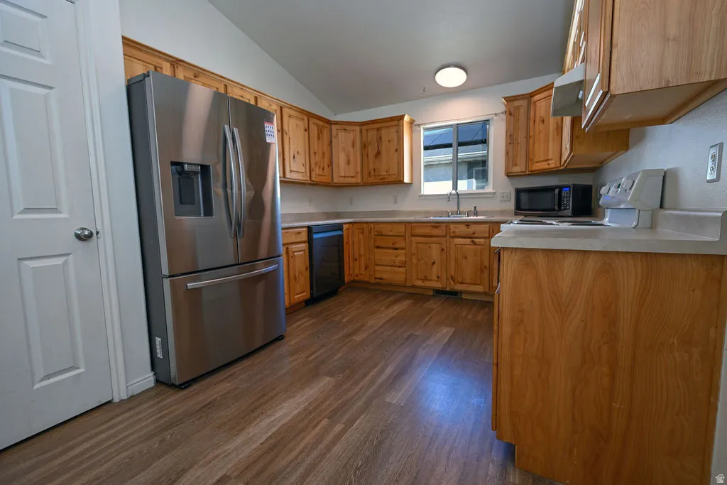 Wood-finish flooring, wood cabinetry, stainless steel refrigerator, white countertops, and a built-in dishwasher