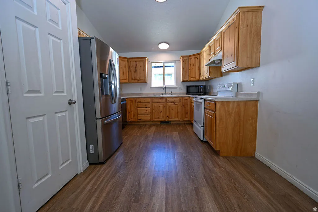 Kitchen featuring wood-finish flooring, natural wood cabinetry, stainless steel refrigerator, built-in microwave, and a white electric range