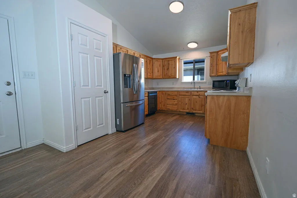 Kitchen featuring wood-finish flooring, vaulted ceilings, natural wood cabinetry, light countertops, and stainless steel appliances
