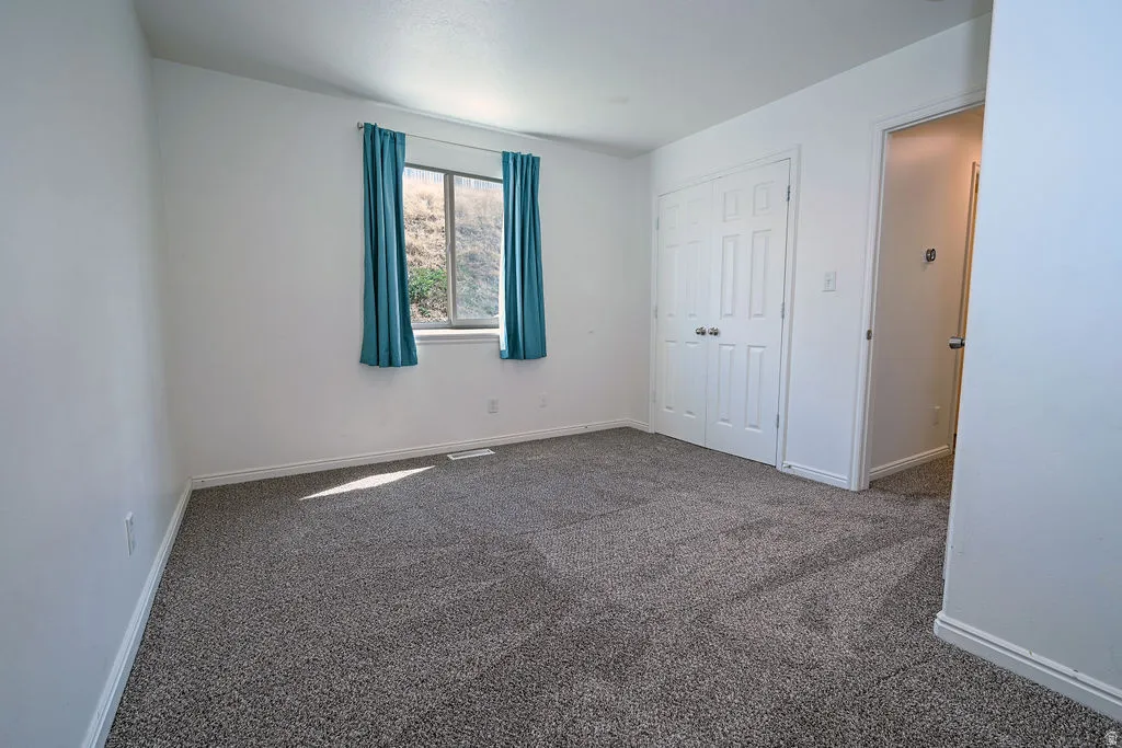 Textured gray carpeting, white walls, double-panel bifold closet doors, and a window with a white frame