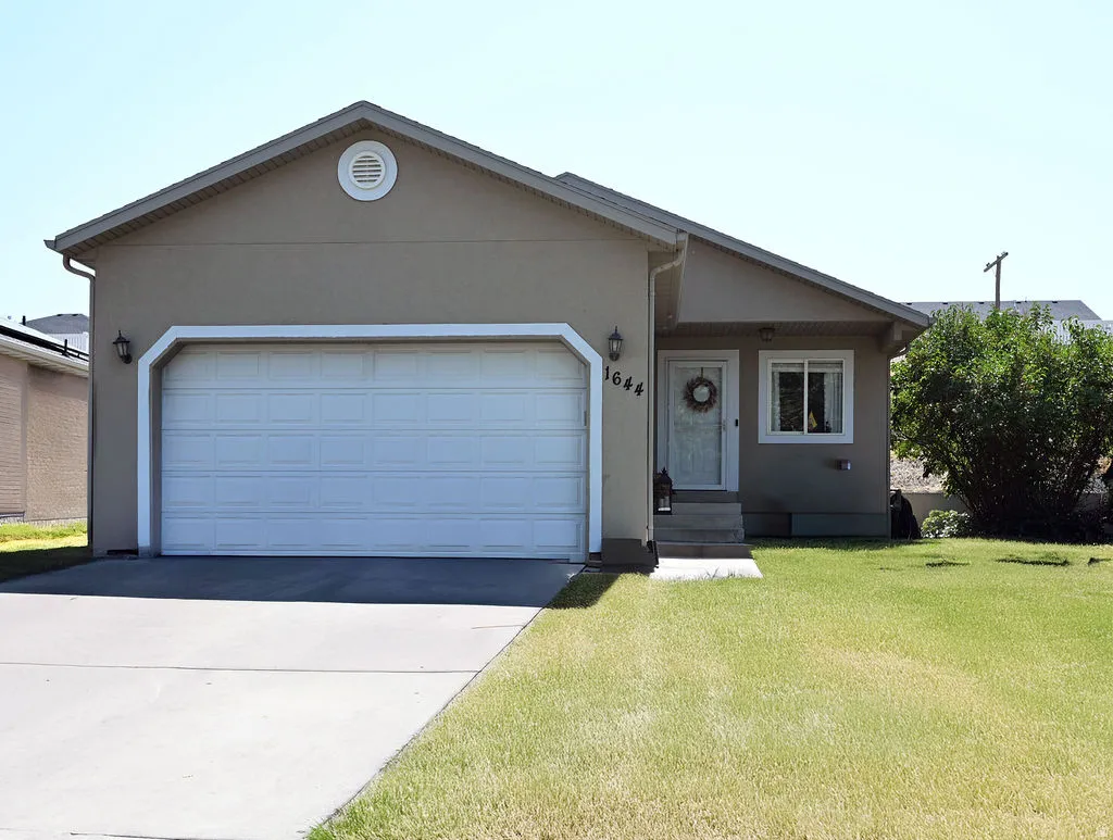 Stucco exterior with a peaked roofline, front-facing garage, concrete driveway, and front lawn