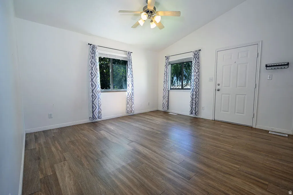 Vaulted ceiling with a ceiling fan, two windows, wood-finish flooring, and a paneled entry door