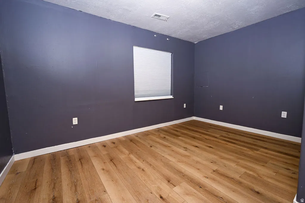 Wood-finish flooring, window with horizontal blinds, wall-mounted electrical outlets, and white trim