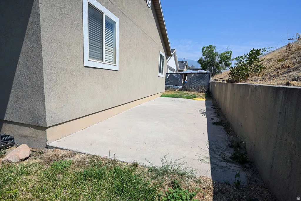 Stucco exterior, white-framed windows, concrete patio, concrete retaining wall, sloped landscape