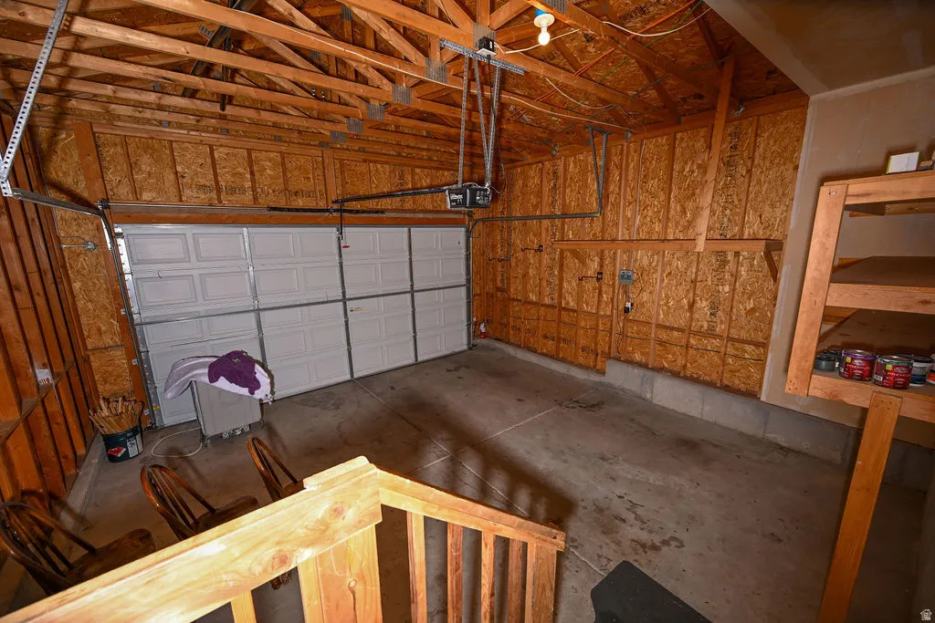 Two-car garage with exposed wood beam ceiling, paneled wood walls, and a concrete floor