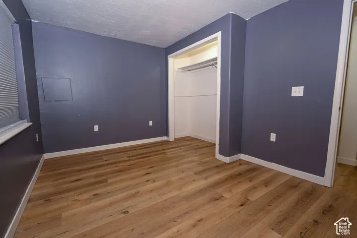 Wood-finish flooring with a neutral tone, built-in closet, and a window featuring horizontal blinds