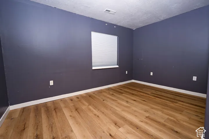 Wood-finish flooring, window with horizontal blinds, wall-mounted electrical outlets, and white trim