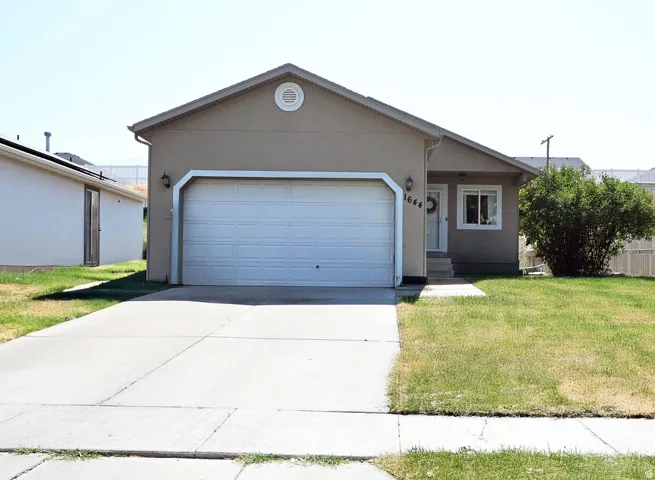 Stucco exterior with a peaked roofline, attached garage, and a concrete driveway
