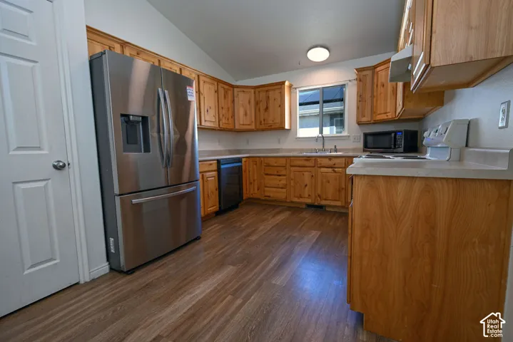 Wood-finish flooring, wood cabinetry, stainless steel refrigerator, white countertops, and a built-in dishwasher