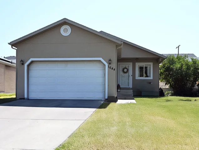 Stucco exterior with a peaked roofline, front-facing garage, concrete driveway, and front lawn