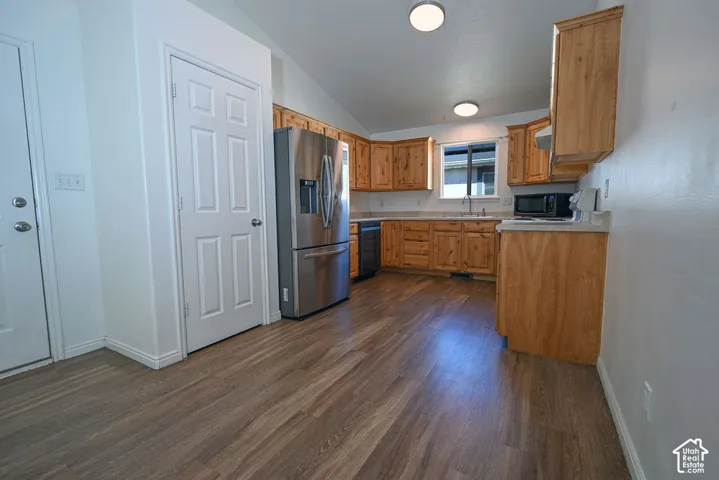 Kitchen featuring wood-finish flooring, vaulted ceilings, natural wood cabinetry, light countertops, and stainless steel appliances