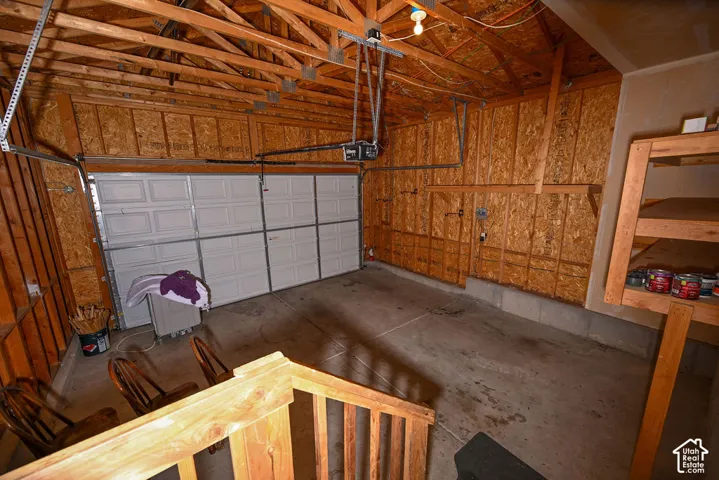Two-car garage with exposed wood beam ceiling, paneled wood walls, and a concrete floor