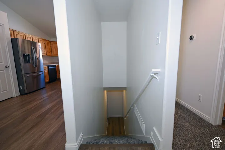 Recessed staircase featuring a white handrail, wood-finish flooring, and light carpeting