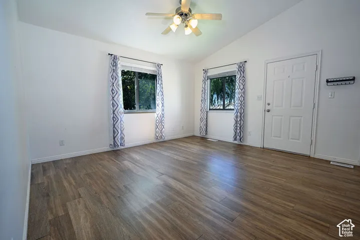 Vaulted ceiling with a ceiling fan, two windows, wood-finish flooring, and a paneled entry door