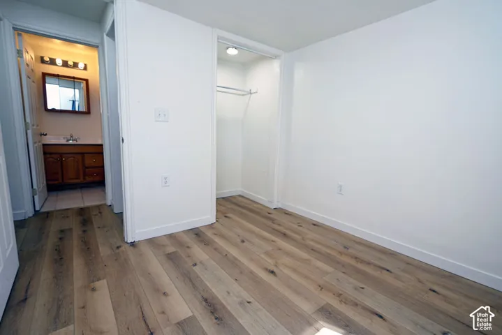 Wood-finish flooring throughout, white painted walls, and an open closet with a built-in hanging rod