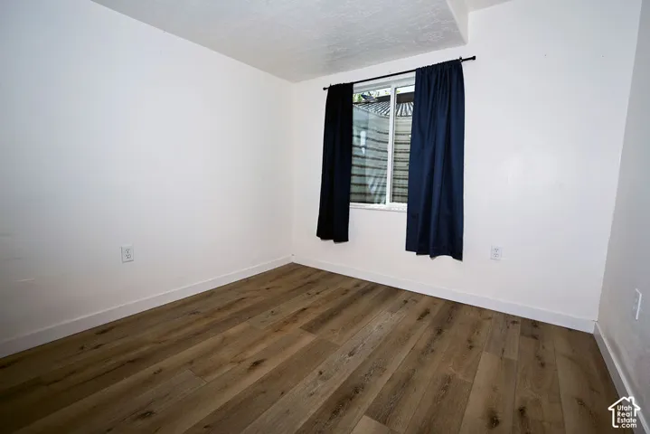Wood-finish flooring with white baseboards, bright white walls, and a window with dark drapery