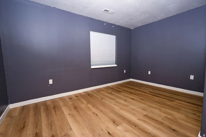 Wood-finish flooring, window with horizontal blinds, wall-mounted electrical outlets, and white trim