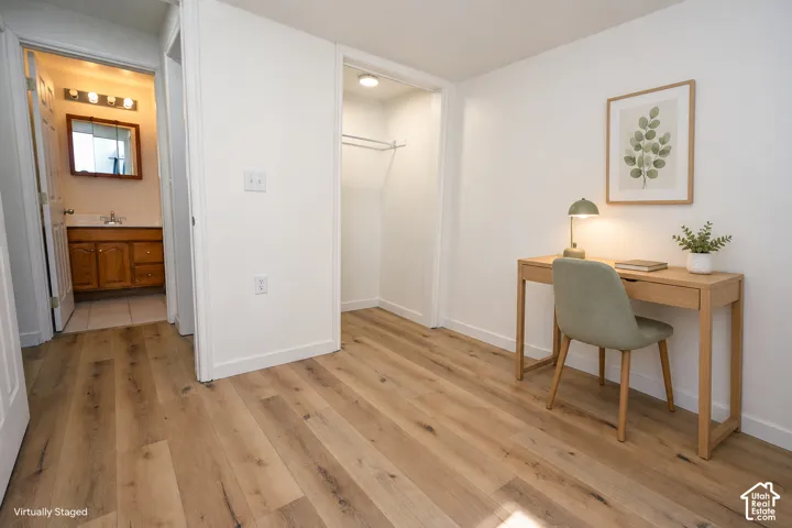 Room featuring wood-finish flooring, a reach-in closet with a built-in rod, and an attached bathroom with a wood vanity and overhead lighting
