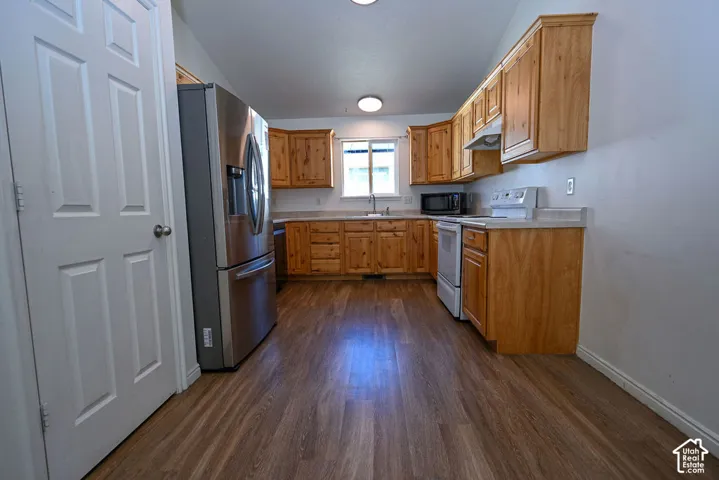 Kitchen featuring wood-finish flooring, natural wood cabinetry, stainless steel refrigerator, built-in microwave, and a white electric range