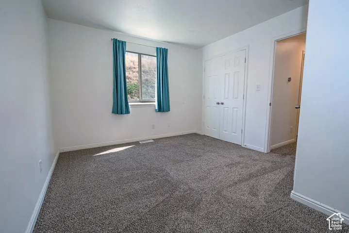 Textured gray carpeting, white walls, double-panel bifold closet doors, and a window with a white frame