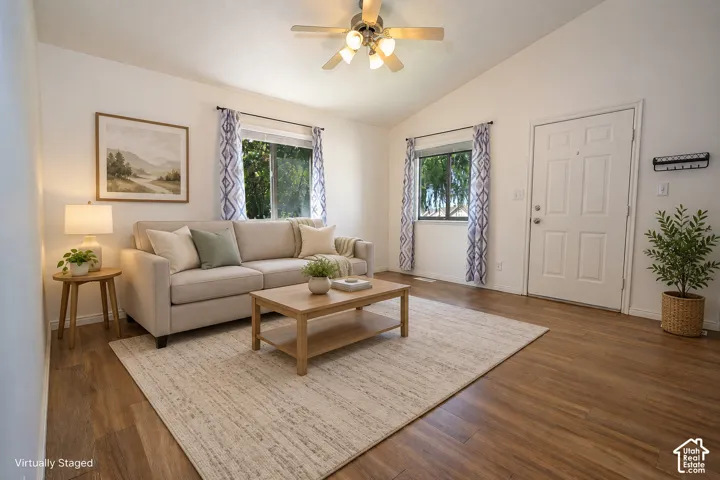 Living space featuring vaulted ceilings, wood-finish flooring, dual windows, and an attached ceiling fan with integrated lighting