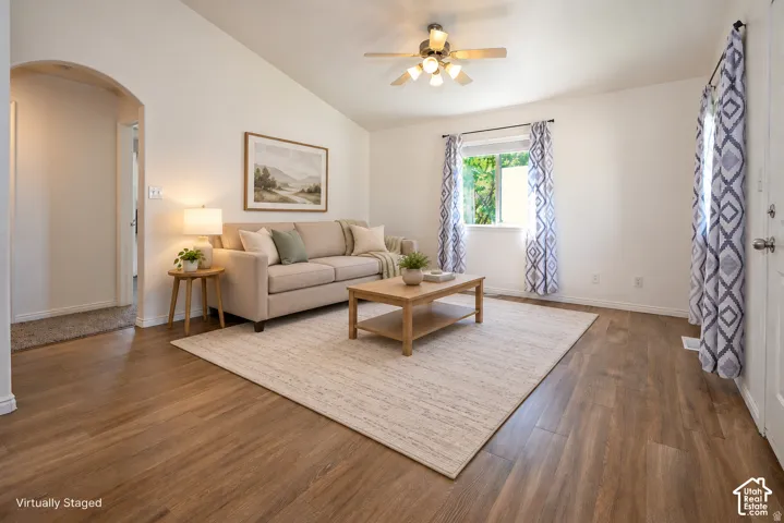 Living area featuring wood-finish flooring, vaulted ceilings, an arched doorway, and a ceiling fan with integrated lighting