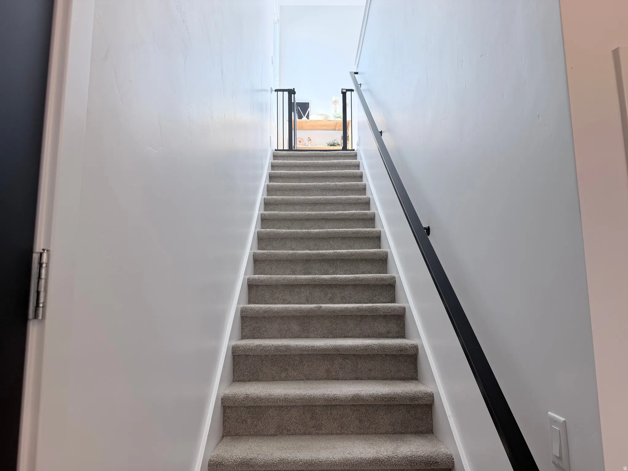 Carpeted staircase with white risers and a black handrail