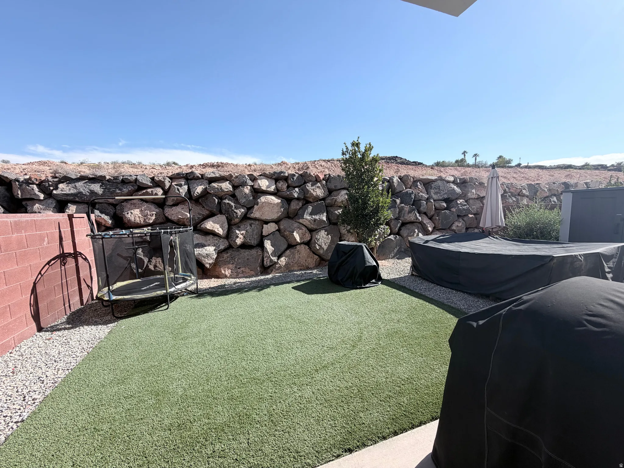 Backyard featuring a stone retaining wall, artificial turf, and a red brick wall