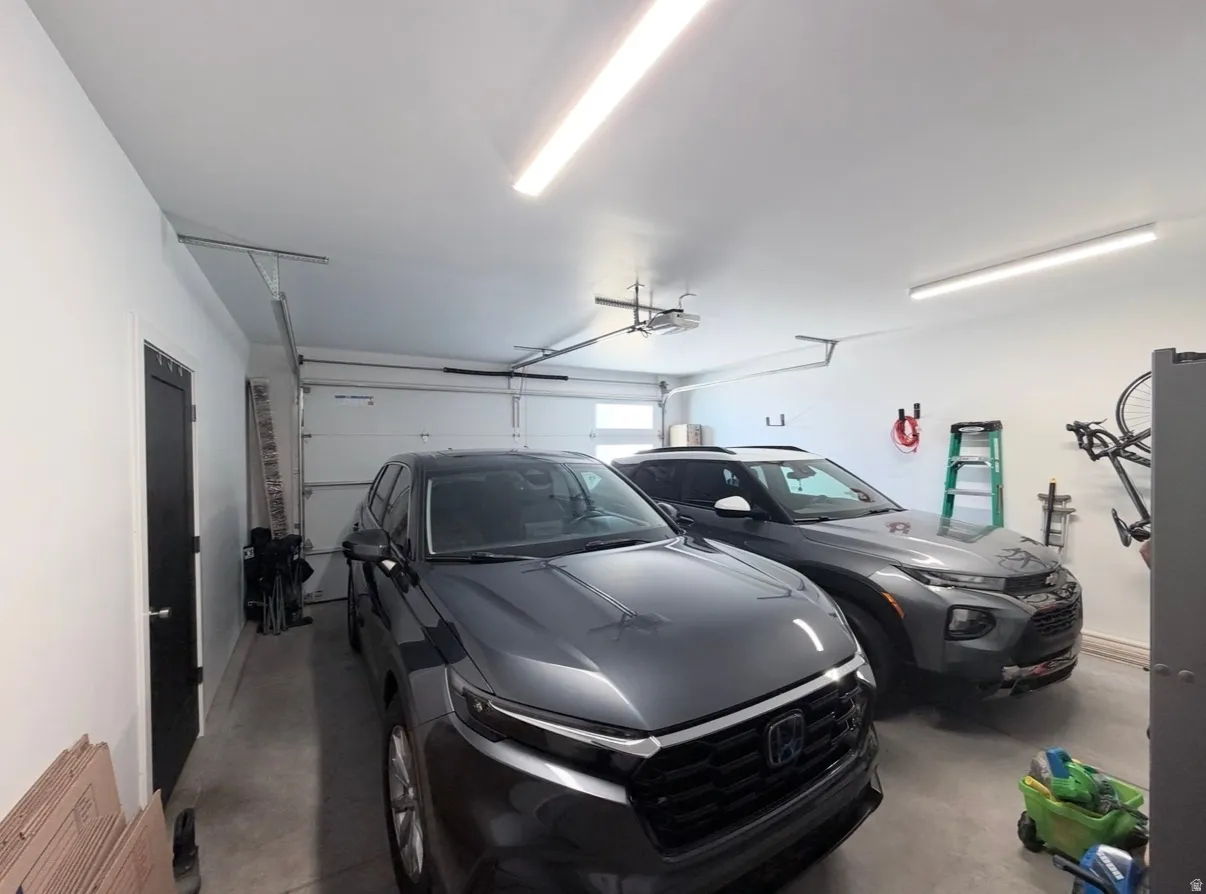 Two-car garage with white walls, concrete flooring, and overhead strip lighting