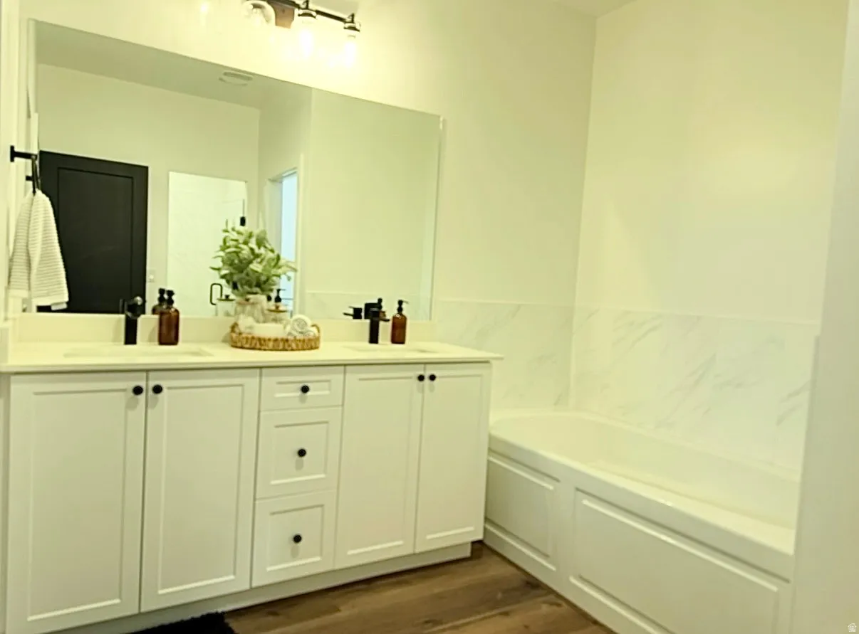 Dual basin vanity with solid surface countertop, wood-finish flooring, built-in bathtub, and marble-look wall tile