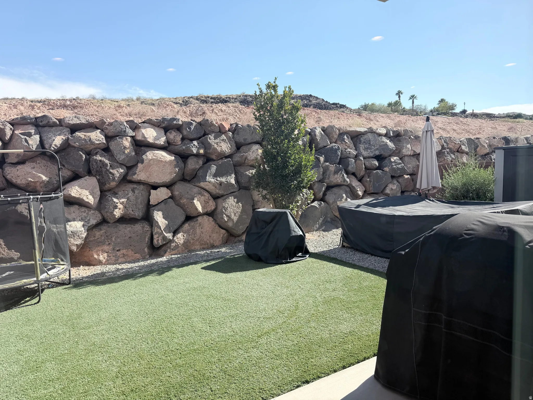 Manicured artificial turf, gravel hardscaping, and a robust rock retaining wall