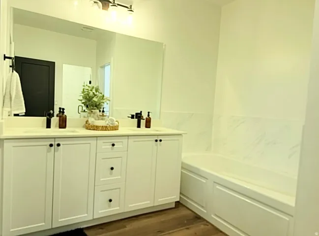 Dual basin vanity with solid surface countertop, wood-finish flooring, built-in bathtub, and marble-look wall tile