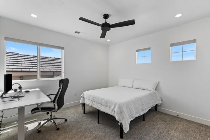 Recessed lighting, ceiling fan, and multiple windows provide ample illumination, complemented by neutral wall tones and textured carpeting