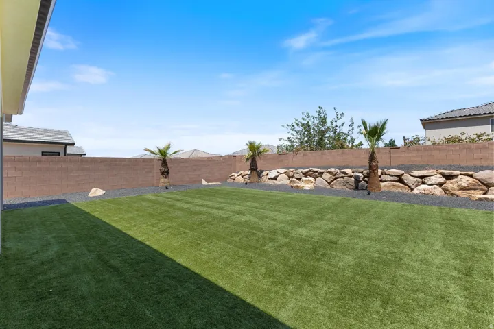 Expansive backyard featuring artificial turf, a block privacy wall, decorative rock landscaping, and mature palm trees