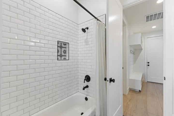 Spa-inspired bathroom featuring crisp white subway tile walls, a chrome rainfall showerhead with matching valve controls, and a classic white bathtub with integrated fixtures