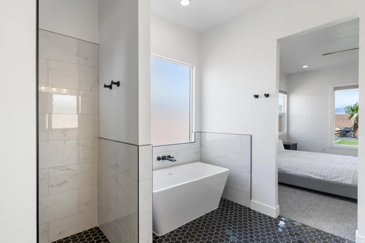 Spa-inspired primary bathroom featuring a freestanding soaking tub, walk-in shower with linear tile surround and matte black hardware, hex-tile flooring, and abundant natural light from a large window