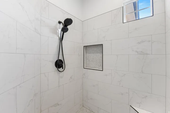 Shower with large format white tile walls, recessed niche with mosaic tile, matte black shower fixtures, and an upper window