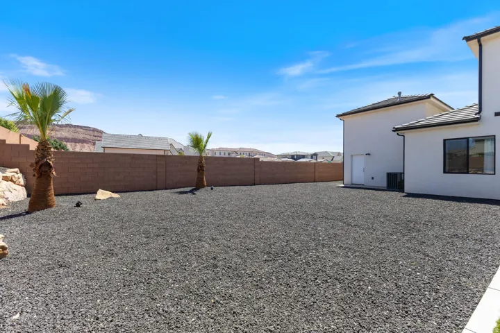 Expansive backyard featuring dark gravel landscaping, two mature palm trees, and a block perimeter wall
