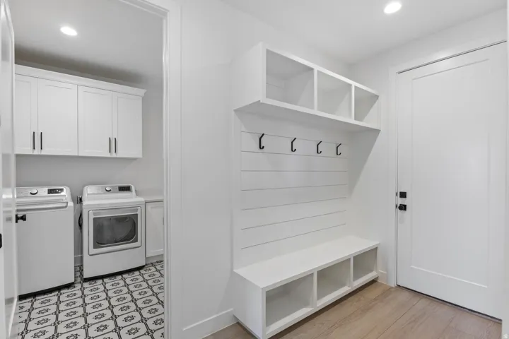 Mudroom and laundry room featuring built-in cubbies with open shelving, wall-mounted hooks for coats and accessories, shiplap accent wall, recessed lighting, and direct access to an adjacent laundry space equipped with front-load washer and dryer