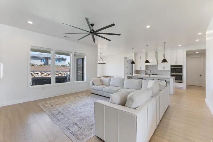Open-concept living area featuring a modern black ceiling fan, recessed lighting throughout, and wide windows with natural light