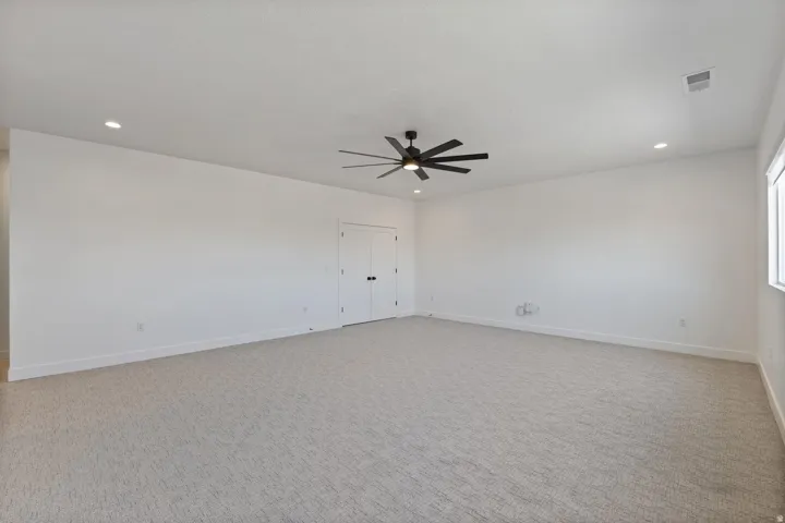 Spacious bedroom featuring neutral carpet flooring, recessed ceiling lighting, a ceiling fan with brushed metal finish, and abundant natural light from a generous window