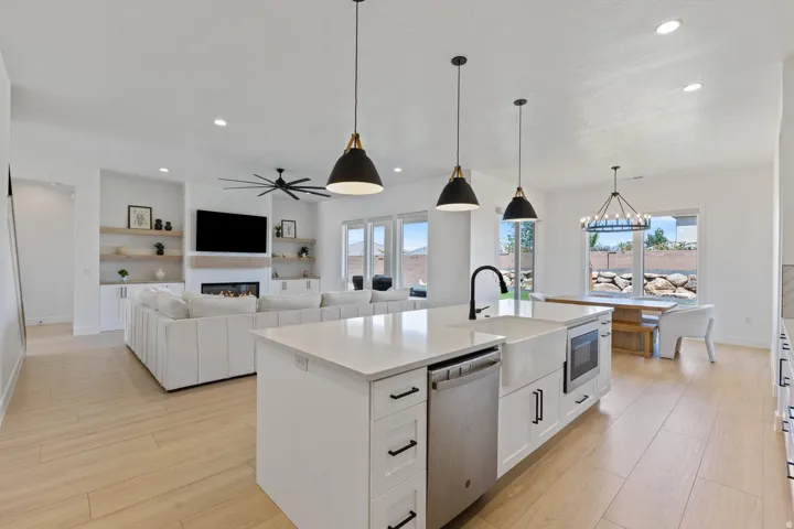 Open-concept kitchen and living area featuring a large center island with stainless steel appliances, white cabinetry, pendant lighting, wood-finish flooring throughout, and abundant natural light from multiple windows and skylights