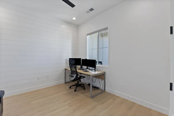 Spacious room featuring a shiplap accent wall, light wood-finish flooring, a contemporary ceiling fan, and a transom window
