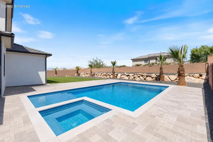 Resort-style backyard oasis featuring a geometric saltwater pool with integrated spa, travertine-look paver decking, mature palm landscaping, and open lawn space