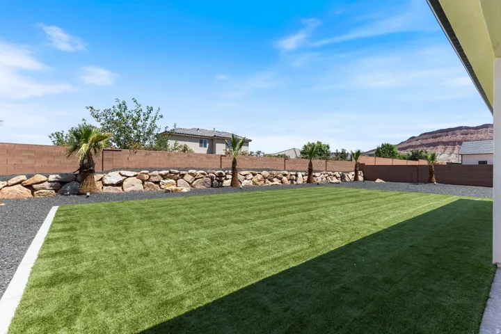 Expansive backyard showcasing a professionally manicured lawn with linear striping pattern, mature palm trees, and decorative rock landscaping