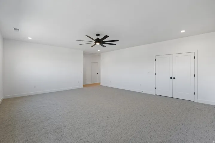Spacious room featuring light gray carpeting, recessed lighting, and a modern ceiling fan
