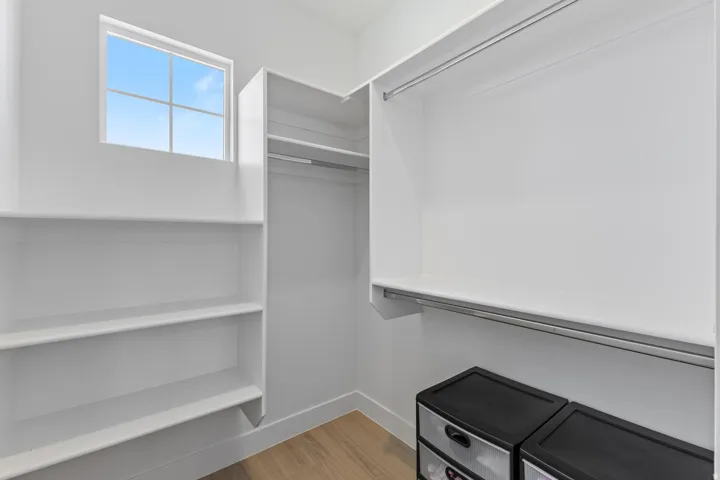 Recessed window, wood-finish flooring, built-in shelving, white walls, and built-in closet rods